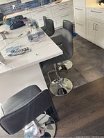 Three adjustable counter stools with gray fabric upholstery and chrome metal bases shown at a kitchen counter.