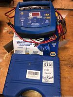 Photo showing the NAPA battery charger resting on its original box along with a blue carrying case labeled as brake bleeder and battery charger.