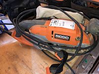 Ridgid belt sander viewed from the side showing the logo, power cable, and body with wear.
