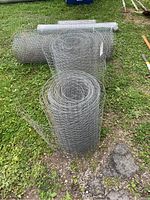 Five rolls of chicken wire standing vertically outdoors on grass and gravel.