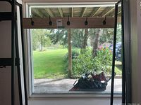 Front view of coat rack with six hooks, wooden top bench and black metal frame beside a sliding glass door