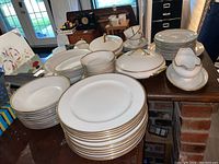 Overall view of multiple stacks of white porcelain dishes with gold rims displayed on wooden table.