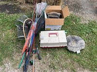 Full view of fishing rods, nets, box of decoys, bait buckets, tackle box, and camo bag arranged on grass ground.