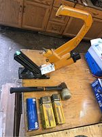Overview of the Bostitch hardwood floor nailer with nails and mallet on a wooden table, showing the nailer in detail along with the nail boxes and mallet.