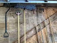 Garden tools including hand tiller, rake, hoe, shovel with wooden handles mounted on wall