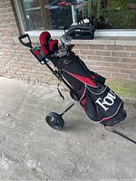 Golf bag with clubs and pull caddy outdoors on cement ground by brick wall
