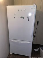 Full view of the white Kenmore refrigerator with freezer on bottom, showing refrigerator door with hooks and magnets attached.
