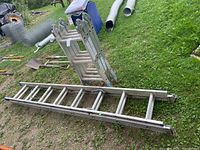 Two aluminum ladders on the ground: one multi-position folding ladder, one standard extension ladder.