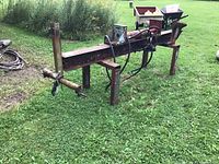 Full side view of hydraulic log splitter on grass showing frame, cylinder, legs and wedge head.