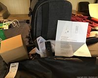 Photo of the gray camera backpack bag, boxed item, carry bag, remote control, and instruction sheet laid out on a surface.
