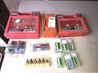 Lot overview showing two red plastic cases with router bit sets, orange box, multiple loose bits in packaging, and white and green-labeled plastic boxes with bits.