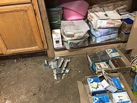 Photo capturing various boxes of screws, brackets, and staples stored on a shelf next to a wooden cabinet.