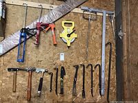 Various hand tools mounted on wood wall including caulking guns, measuring tape, drywall T squares, and crow bars