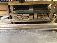Planks of red oak stacked under a workbench.