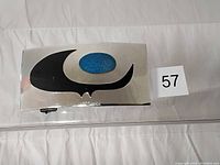 Rectangular metal belt buckle with black and blue enamel design, flat on white background with lot number 57 visible.