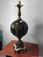 Full view of the vintage table lamp showing green glass spherical body, brass floral decoration, and marble base.