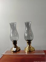 Pair of clear glass candle sticks with brass bases displayed side by side against a plain light background, showing overall shape and condition.