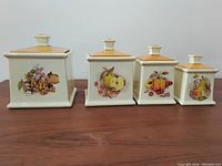 Four ceramic canisters with fruit decals on the front, all lid tops visible