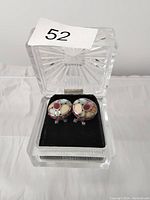 Pair of sterling silver circular clip-on earrings with colorful stone inlays in a clear plastic display box with black velvet inside.