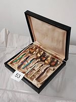 Set of six sterling silver spoons with enamel handles in a black presentation box, showing overall set appearance.