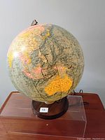 Front and side view of vintage light-up globe showing Asia and Australia on antique-style map, mounted on a dark wooden base with power cord visible.