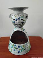 Front view of white ceramic incense burner shaped as figure with smiling face and floral decoration.