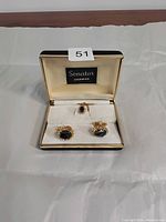 Open box showing pair of gold-tone men's cuff links with large black stone centers, placed in a cushioned display inside a box branded 'Senator Sherman'.