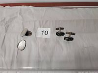 Two pairs of men's sterling silver cuff links displayed on white paper; one pair has a smooth oval design, the other has a black swirl pattern.