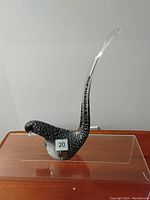 Side view of the Murano glass bird sculpture showing the long curved clear glass tail and black and white speckled body.