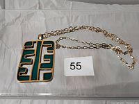 Full view of the vintage necklace showing the gold-tone chain and large rectangular pendant with turquoise inlay and geometric pattern.