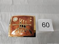 Front of square enamel pin showing abstract organic gold, copper, black, and white design on copper-toned background.