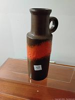Front side of the vase, showing the textured orange band and round handle on a dark brown glossy pottery body.