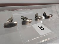 Two pairs of BMW sterling silver cufflinks arranged side by side on a clear surface, highlighting their front with 'BMW' text and logos.