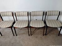 Front view of four teak dining chairs in a row against a wall