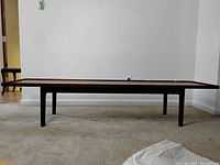 Full front side view of the long teak table showing the tabletop and legs.