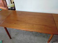 Full view of closed table showing rectangular teak top and round tapered legs