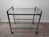 Full view of chrome and glass trolley showing structure and wheels