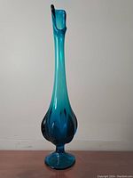 Front angle view of the tall turquoise glass vase showing its elongated neck and bulbous base.