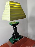 Full view of the vintage lamp with yellow stepped Venetian shade and black bust base on green platform