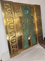 Front view of brass wall plaque showing green patina embossed Chinese symbols in the center and raised geometric side borders.