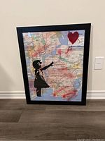 Front view of framed Banksy style graffiti artwork on NYC subway map showing girl reaching towards red heart balloon with red spray paint accents
