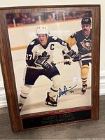 Framed 8x10 color photo of Darryl Sittler on ice in Maple Leafs uniform with autograph, displayed on wooden plaque with engraved nameplate.
