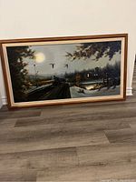 Full view of the large horizontal framed painting showing a night farm and train scene with glowing lights and flying geese.