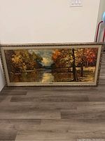 Full view of framed landscape painting showing autumn trees and river.