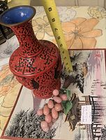 Red cinnabar vase next to measuring tape showing height approx. 11 inches alongside rose quartz grape cluster and woven calendar mat