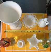 Top view of all glass and milk glass items on yellow cloth, including vase, candy dish, cruet, paperweights, and small dishes.