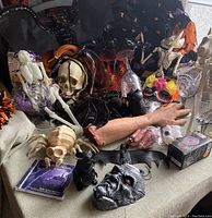 Overview of various Halloween items including skeletons, spiders, plastic skulls, a fake arm, mask, and glasses with skeleton hands on a couch and table.