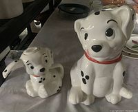 Set of two vintage ceramic Disney 101 Dalmatians pieces, a cookie jar shaped as Rolly and a milk pitcher shaped as Lucky, displayed on a table.