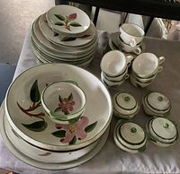 Photo showing dinner plates, side plates, two bowls, cups, and covered sugar bowls with floral designs and green trim.
