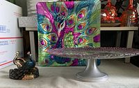 Photo showing round glass dessert platter on metal pedestal stand, colorful square glass peacock platter, and metal peacock-shaped holder.
